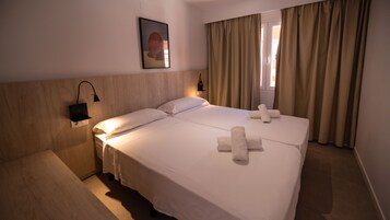 Habitación de hotel con dos camas, cabecera de madera, lámpara de pared y ventana con cortinas.