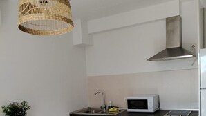 Una cocina moderna con armarios blancos, una campana extractora de acero inoxidable, un microondas y una lámpara colgante de mimbre.