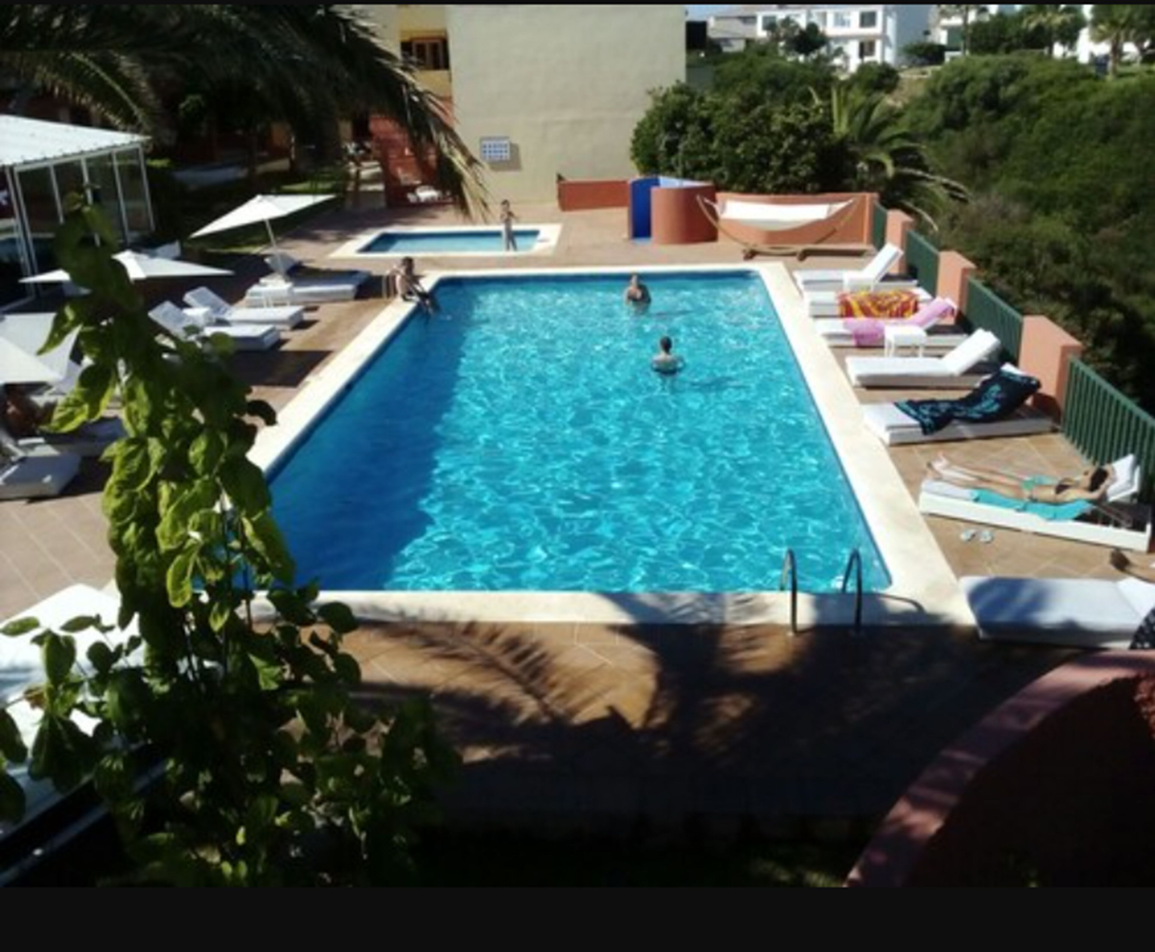 A rectangular pool with a person swimming, surrounded by lounge chairs and umbrellas.