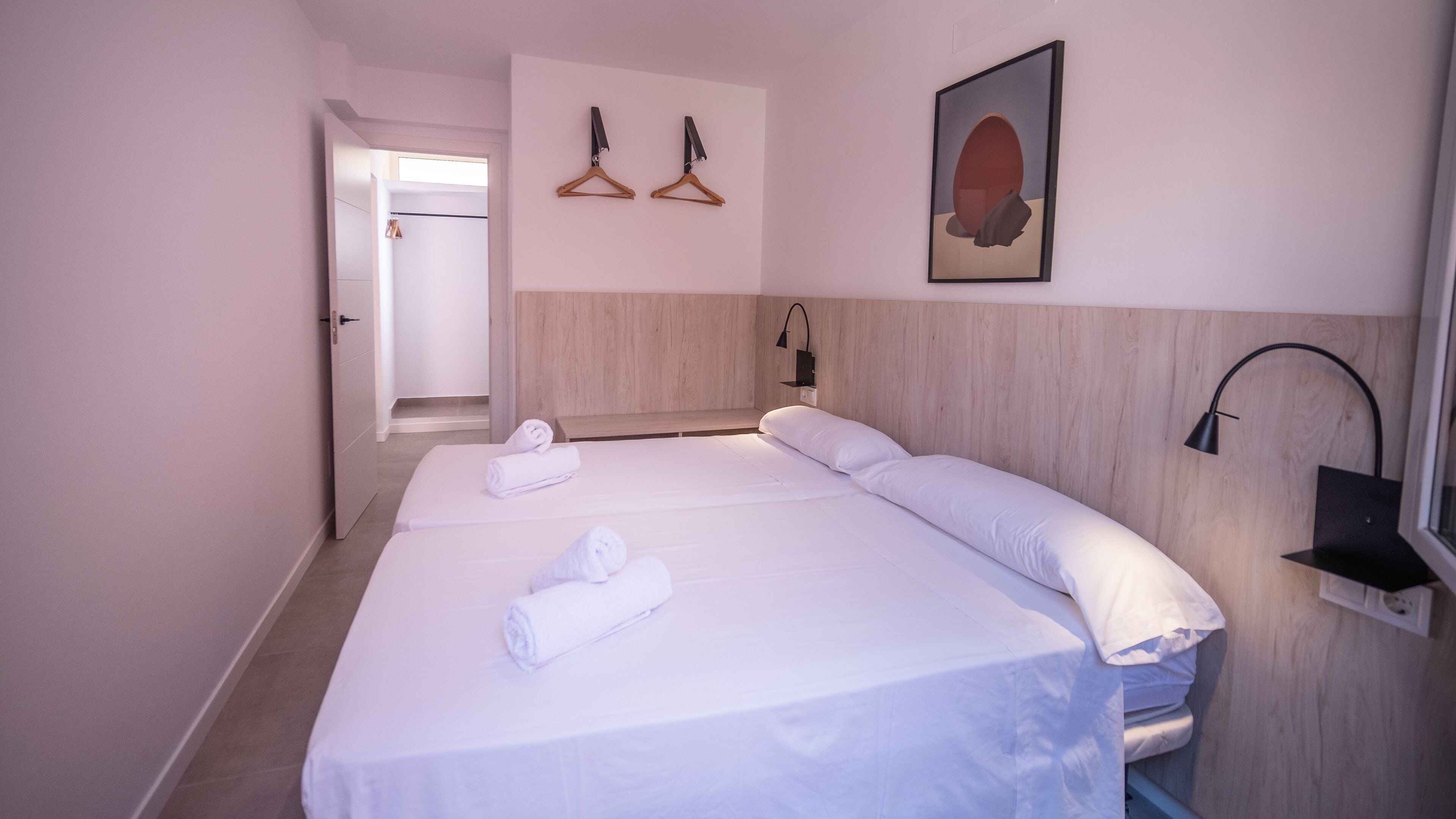 Habitación de hotel con dos camas, cabecero de madera, lámpara de pared y puerta que da a un baño.