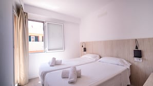 Habitación de hotel con dos camas, una ventana con cortinas, una lámpara de pared y un cabecero de madera.