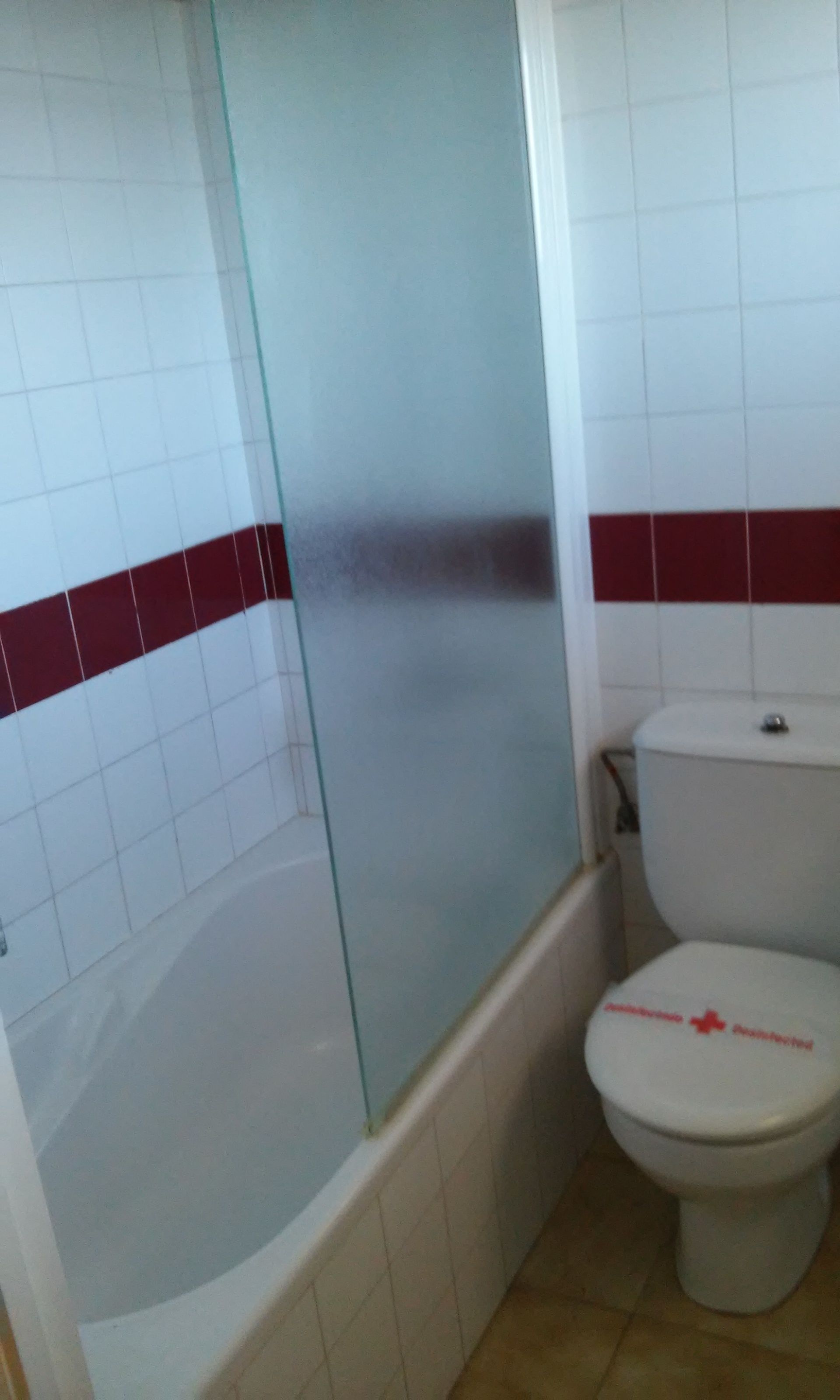 Een badkamer met een glazen douchecabine, een toilet en een betegelde vloer.