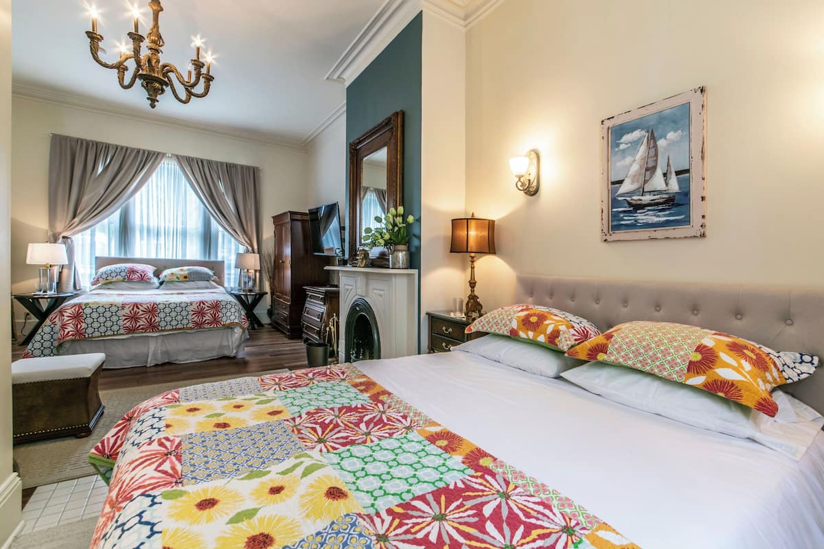 A hotel room with two beds, a chandelier, a fireplace, and a painting of a sailboat.