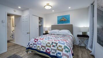 A bedroom with a large bed, a headboard, bedside lamps, a painting on the wall, and a door leading to another room.