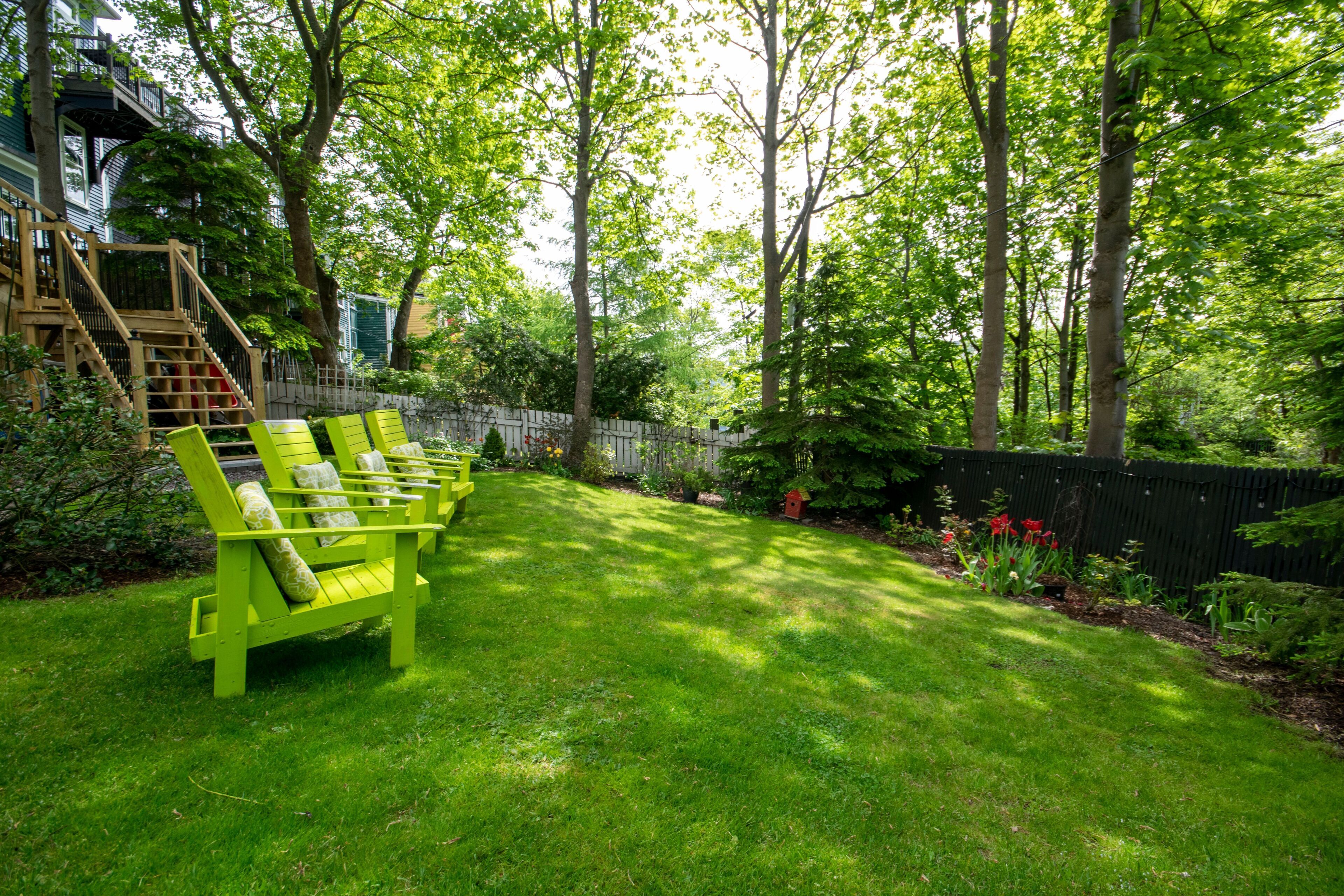 A lush backyard with a wooden staircase leading to a deck, surrounded by tall trees and a well-maintained lawn.