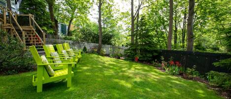A lush backyard with a wooden staircase leading to a deck, surrounded by tall trees and a well-maintained lawn.