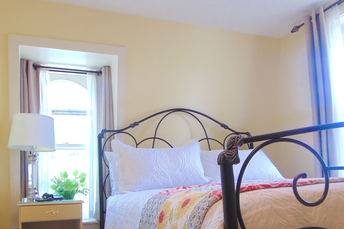 A bed with a metal frame, a bedside table with a lamp, and a window with curtains.