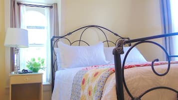 Una cama con estructura metálica, una mesita de noche con lámpara y una ventana con cortinas.