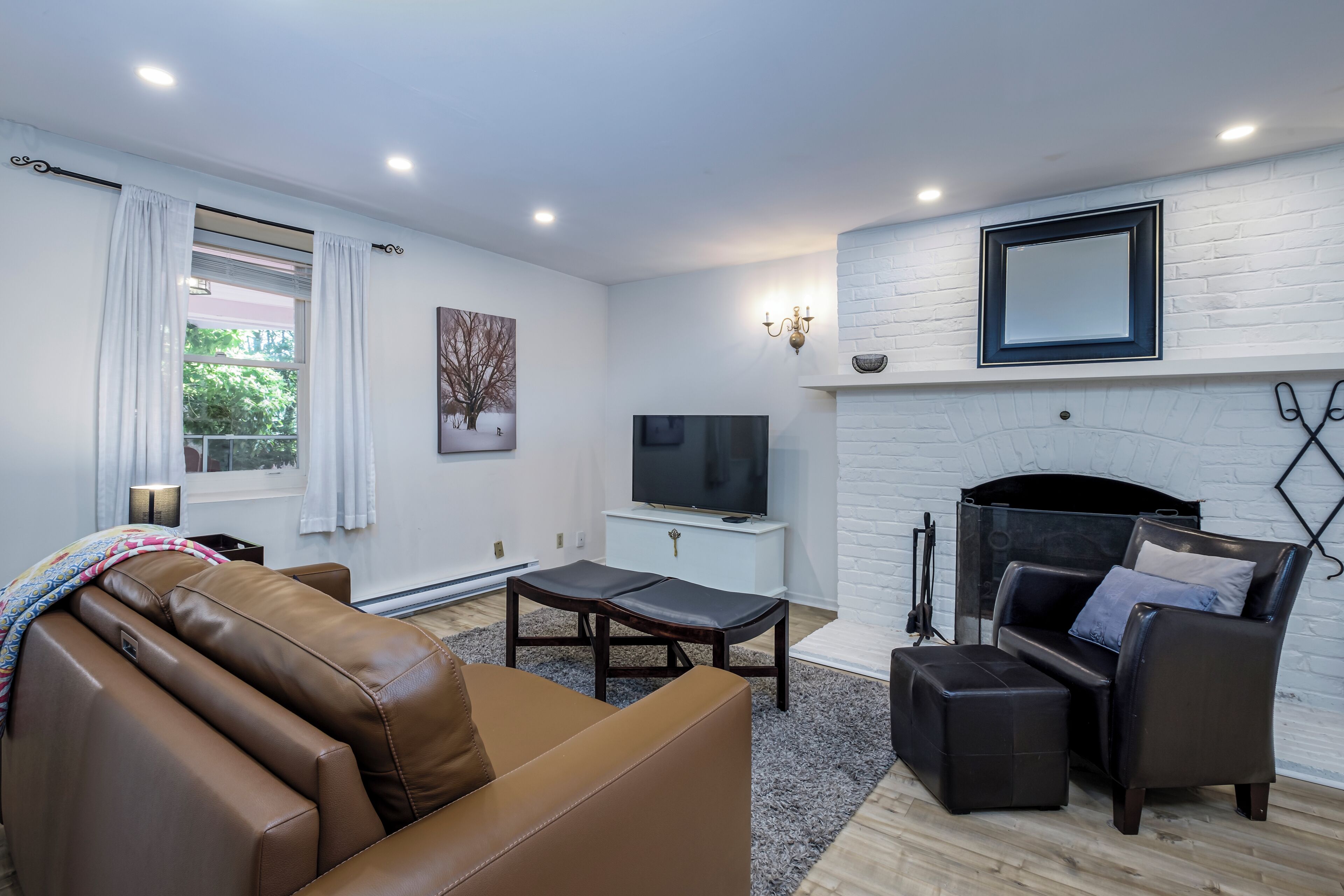 Uma sala de estar moderna com sofá de couro, televisão, lareira e uma janela grande com cortinas.