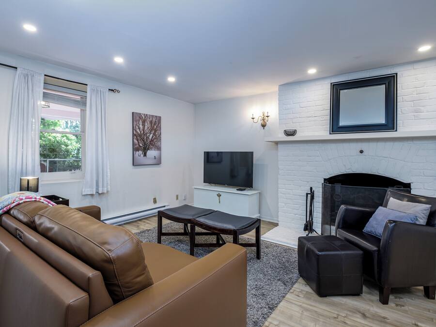 Uma sala de estar moderna com sofá de couro, televisão, lareira e uma janela grande com cortinas.
