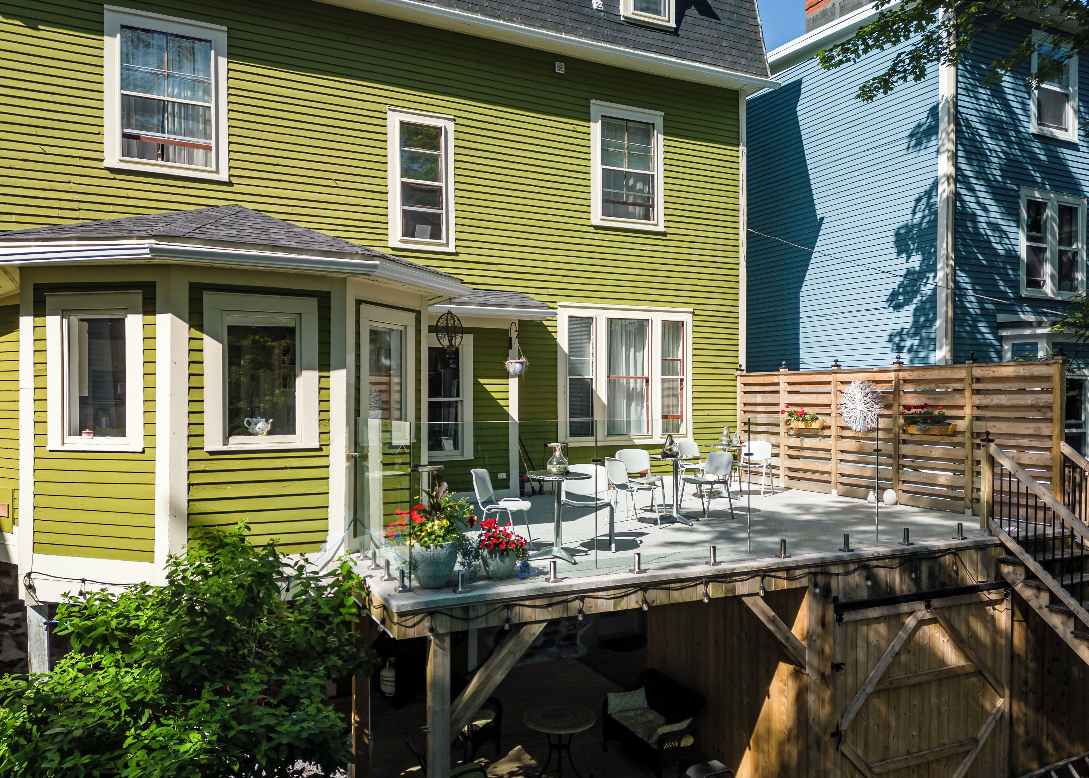 A green house with a covered patio, outdoor seating, and a wooden deck.