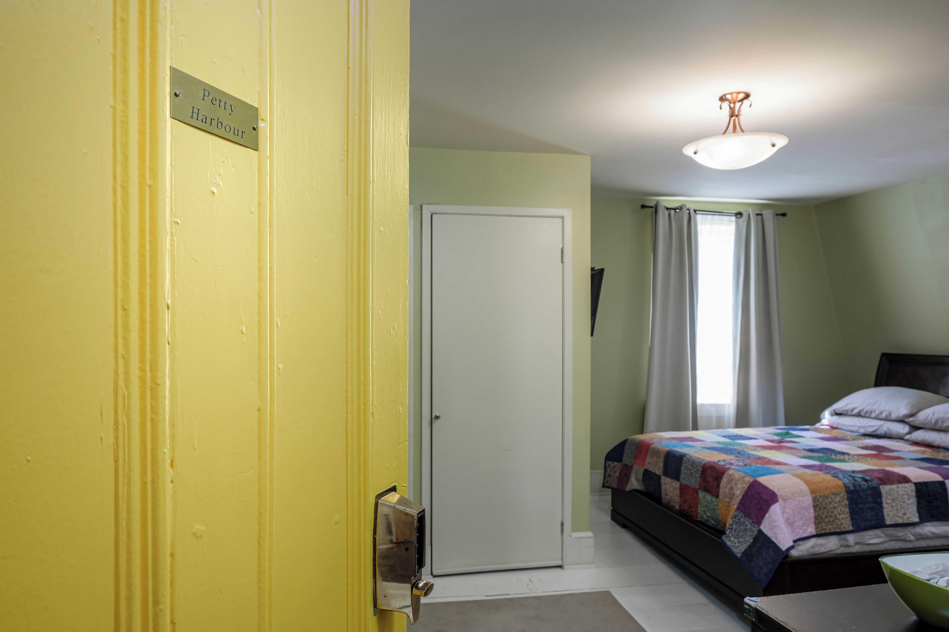 A room with a bed, a nightstand, a door with a sign, and a window with curtains.