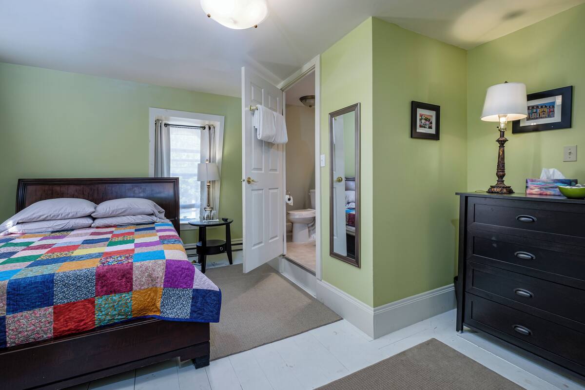 A bedroom with a bed, dresser, and a door leading to a bathroom.