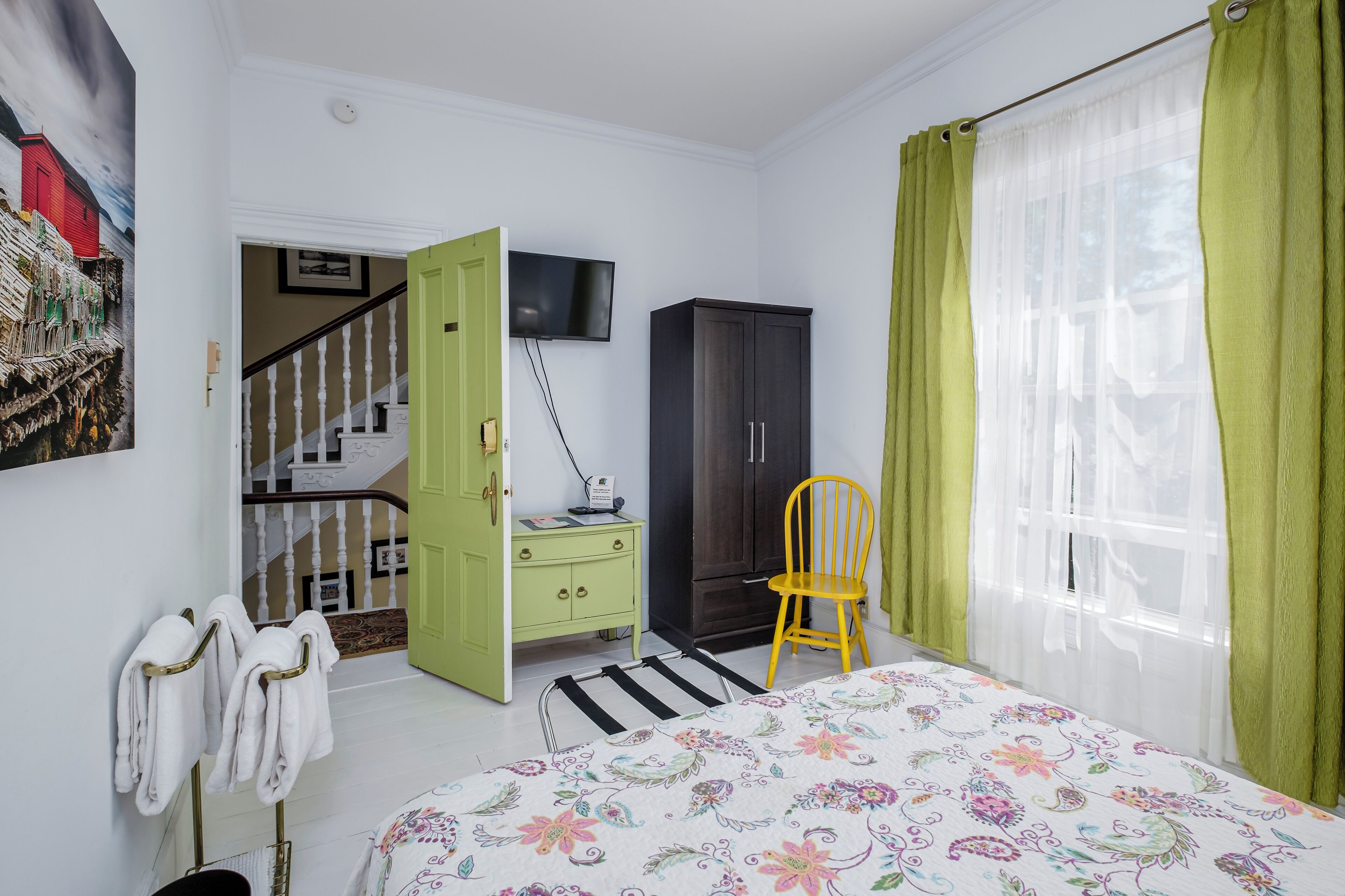 Una camera da letto con un letto, un armadio verde, una televisione, una sedia gialla e una scala che conduce a un'altra stanza.