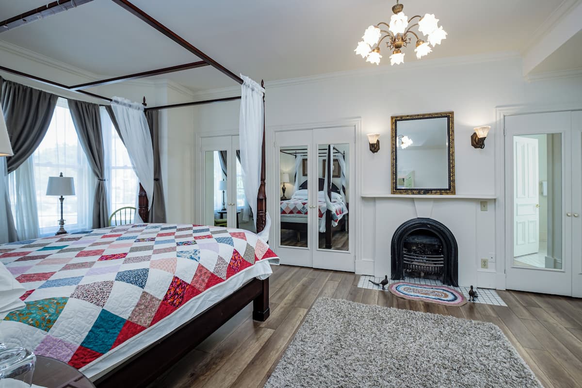 A spacious bedroom with a four-poster bed, a fireplace, and a large mirror.
