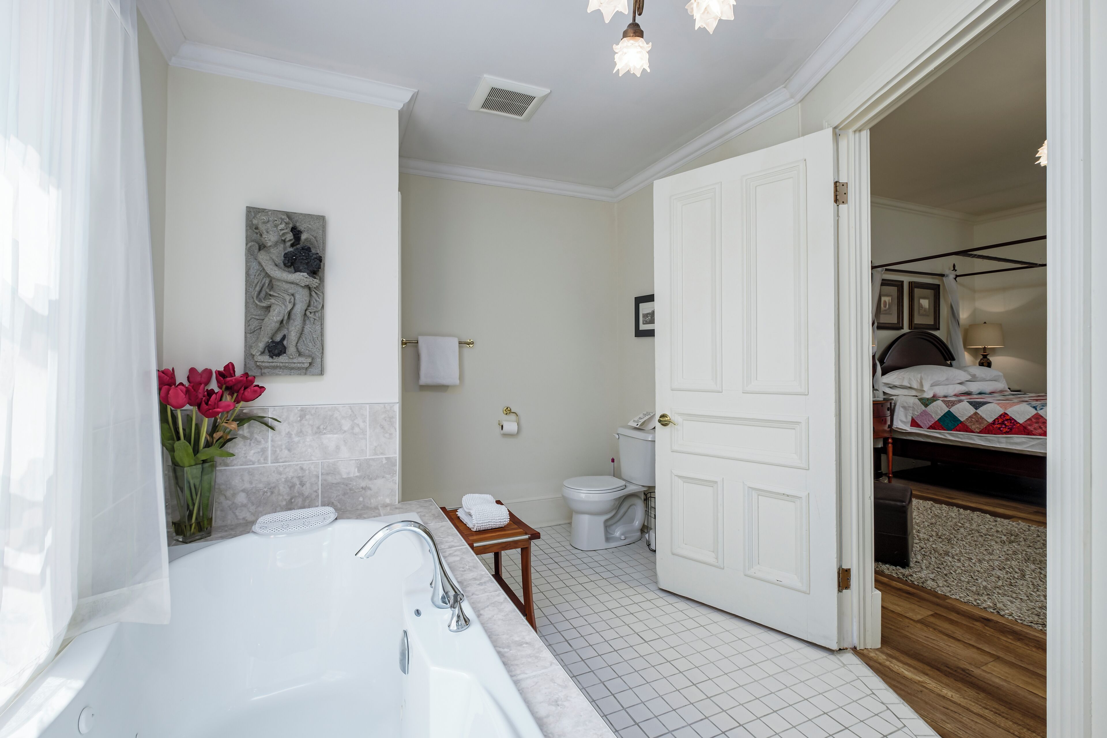 Un baño con bañera, inodoro y una puerta que da a un dormitorio.