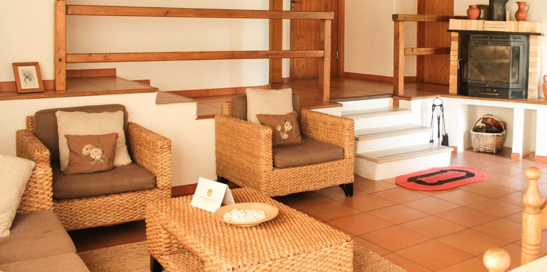 Uma sala de estar acolhedora com móveis de vime, lareira e escada para um andar superior.