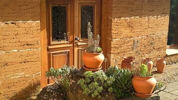 A rustic building with a tiled roof and a wooden door. There are terracotta pots with plants on a rock in front of the door.