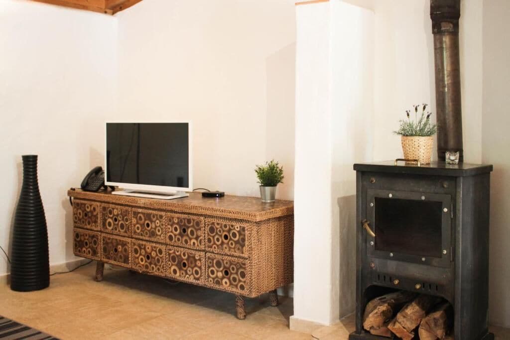 A living room with a TV on a patterned cabinet, a black vase, and a wood-burning stove.