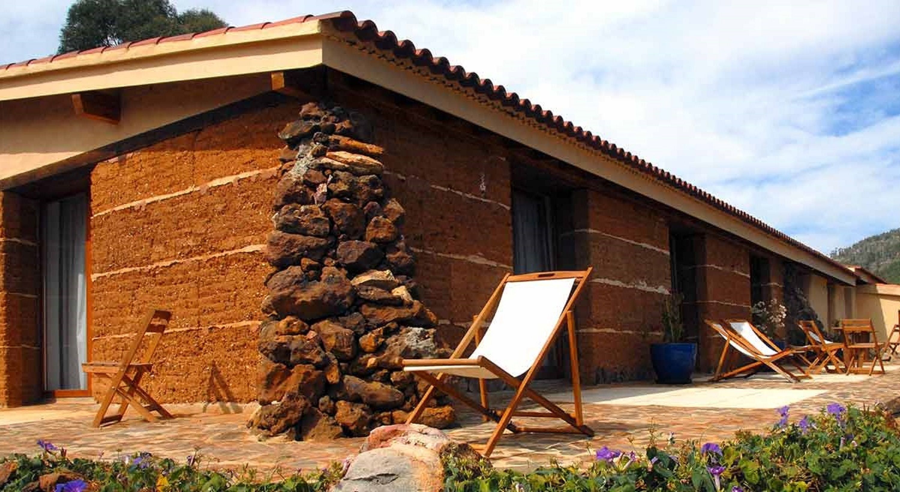 Een gebouw van steen met een pannendak, een stenen muur en een terras met loungestoelen.