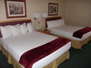 A hotel room with two beds, each with white linens and a red throw blanket. There are two wall-mounted lamps, and the room has a simple, clean design with framed artwork on the walls. - Rocky Inn Express (Rocky Mountain House)