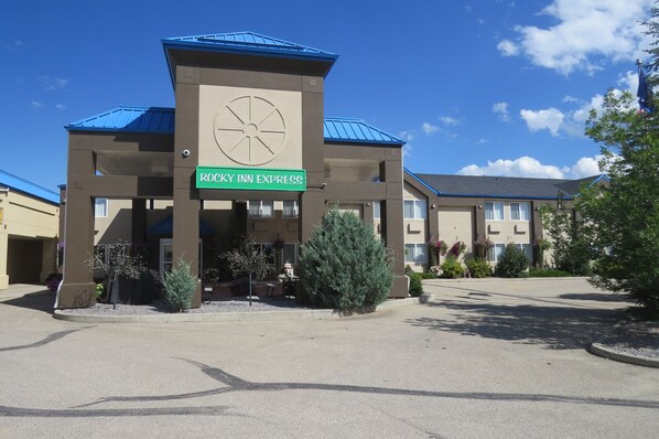 A Rocky Inn Express building with a clock, outdoor seating, and a parking lot. - Rocky Inn Express (Rocky Mountain House)