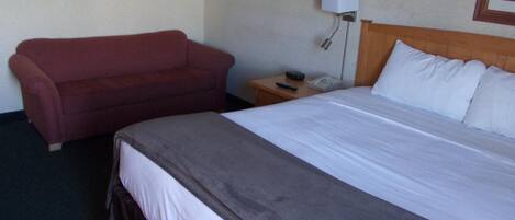 A hotel room with a bed, a red sofa, a nightstand with a lamp, and a framed picture on the wall.
