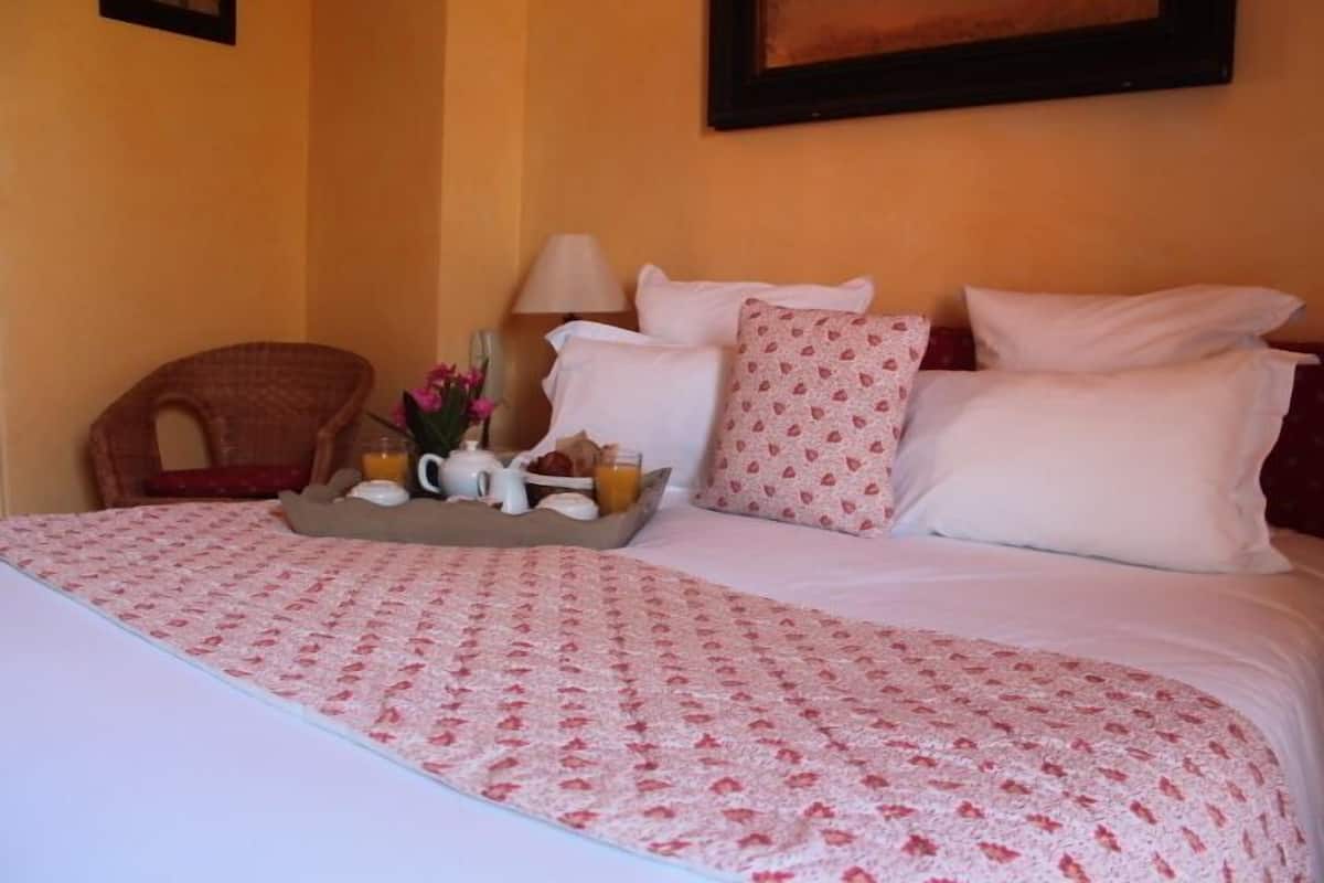 A neatly made bed with a pink and white patterned bedspread, a tray with breakfast items, and a wicker chair beside the bed.