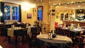 A restaurant with tables set for dining, a bar area, and a kitchen visible in the background. - L'Auberge des Glycines (Hyères)