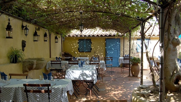 An outdoor dining area with tables and chairs, a blue door, and lanterns on the wall. - L'Auberge des Glycines (Hyères)