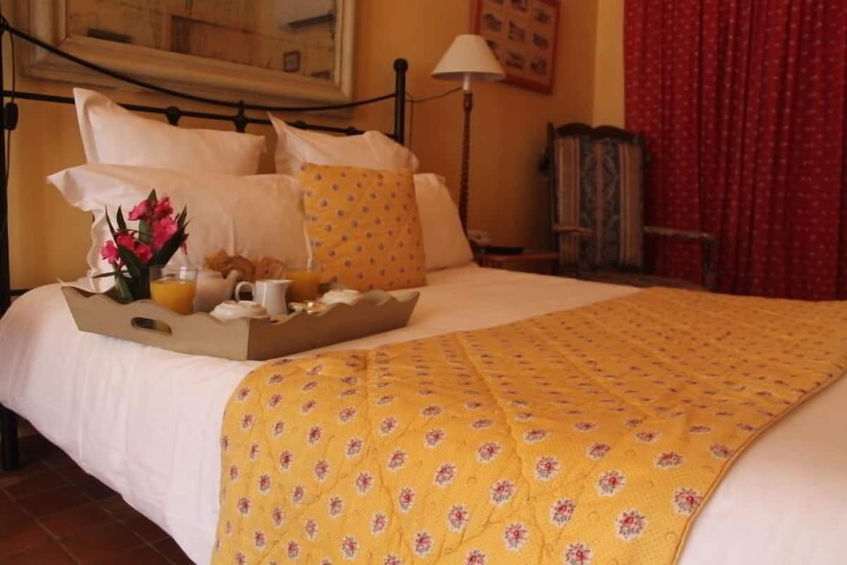 A neatly made bed with a yellow floral bedspread, a tray with breakfast items, and a vase of flowers.