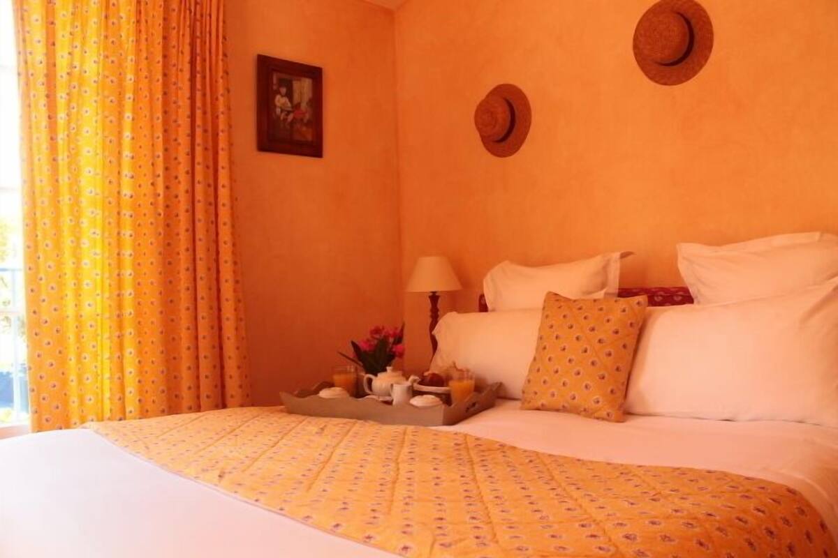 A bed with a floral-patterned bedspread, a tray with breakfast items, and two wall-mounted hats.