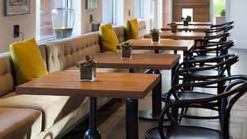 A restaurant interior with long tables, cushioned seating, and black chairs.