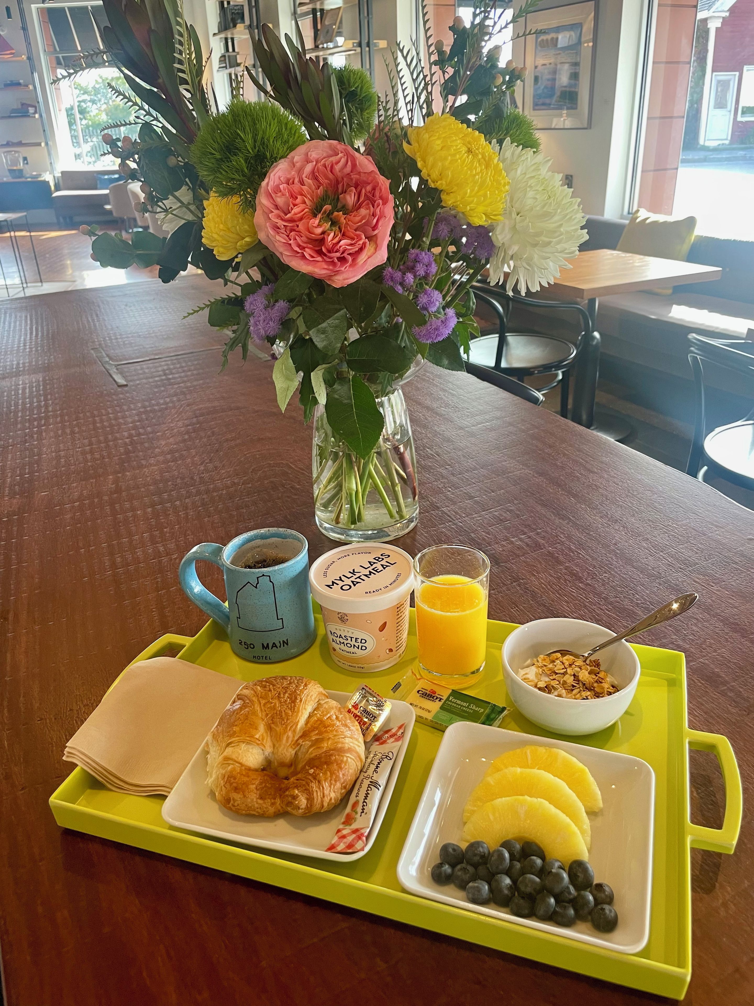 A breakfast tray with croissants, yogurt, orange juice, and a vase of flowers.