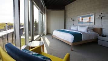 Quarto de hotel moderno com uma cama grande, uma mesinha redonda, uma poltrona amarela e uma varanda com vista para a cidade.