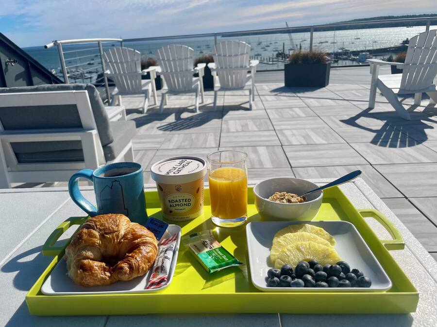 A breakfast tray with croissant, orange juice, yogurt, and blueberries on a terrace with chairs and a view of the water.