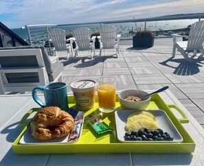 A breakfast tray with croissant, orange juice, yogurt, and blueberries on a terrace with chairs and a view of the water. - 250 Main Hotel (Rockland)