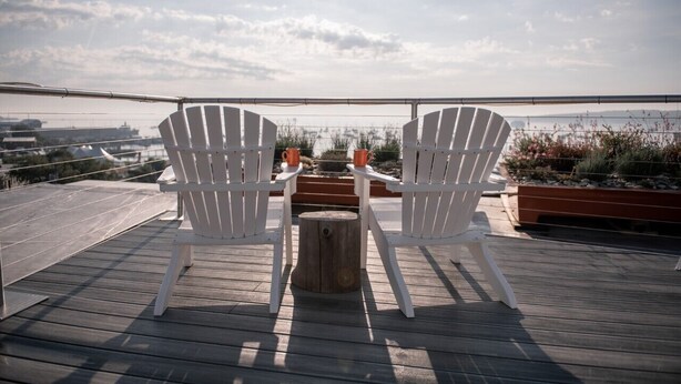 Two white Adirondack chairs facing a wooden deck with a view of the city skyline. - 250 Main Hotel (Rockland)