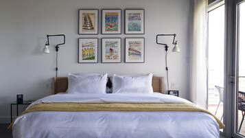 Ein Hotelzimmer mit einem großen Bett, zwei Nachttischen, einem Fenster mit Blick und sechs gerahmten Bildern an der Wand.