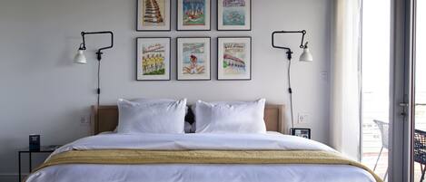 A hotel room with a large bed, two bedside tables, a window with a view, and six framed pictures on the wall.
