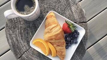 A white plate with a croissant, strawberries, blueberries, and orange slices on a wooden table.
