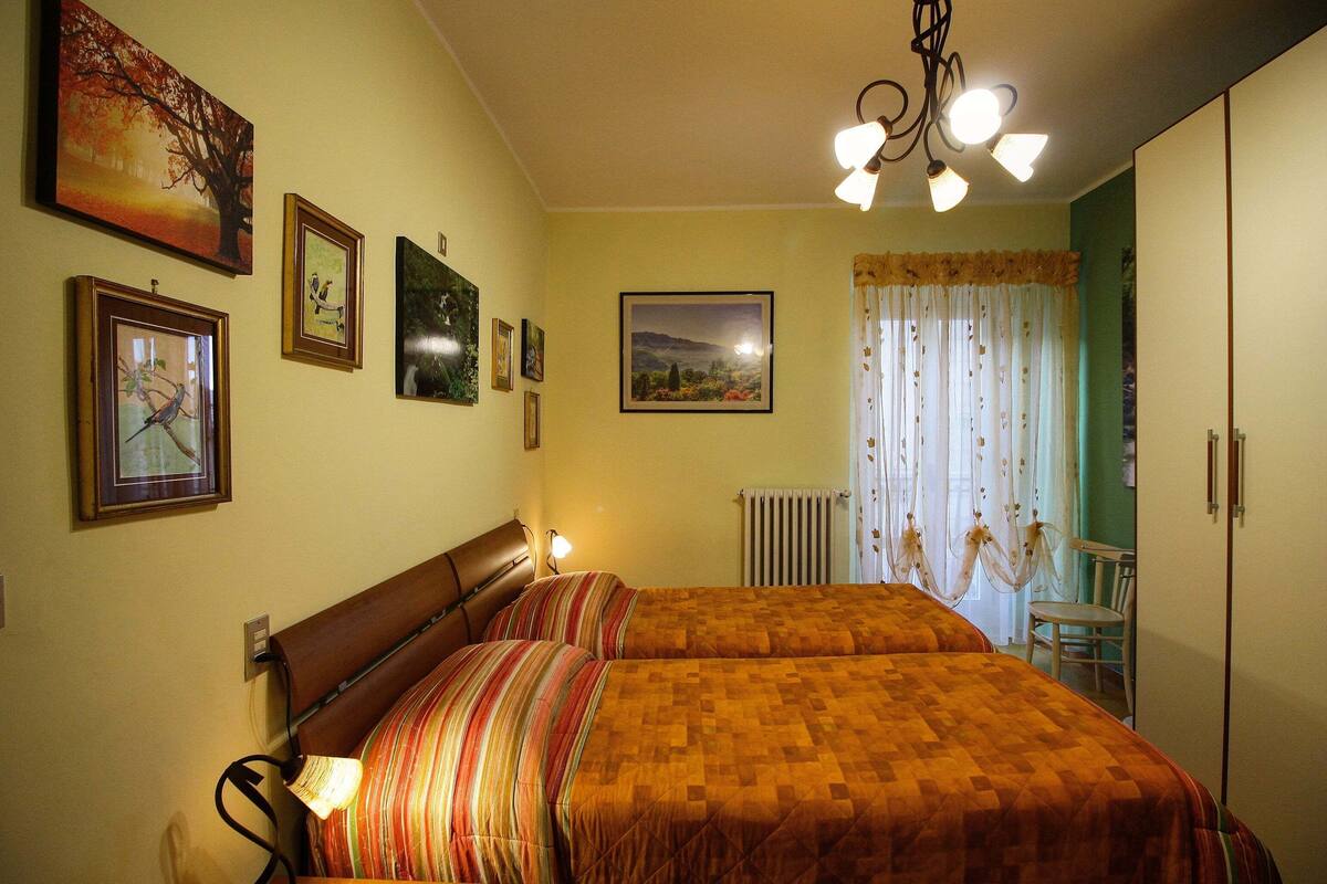A bedroom with two beds, a radiator, a chair, and a table.
