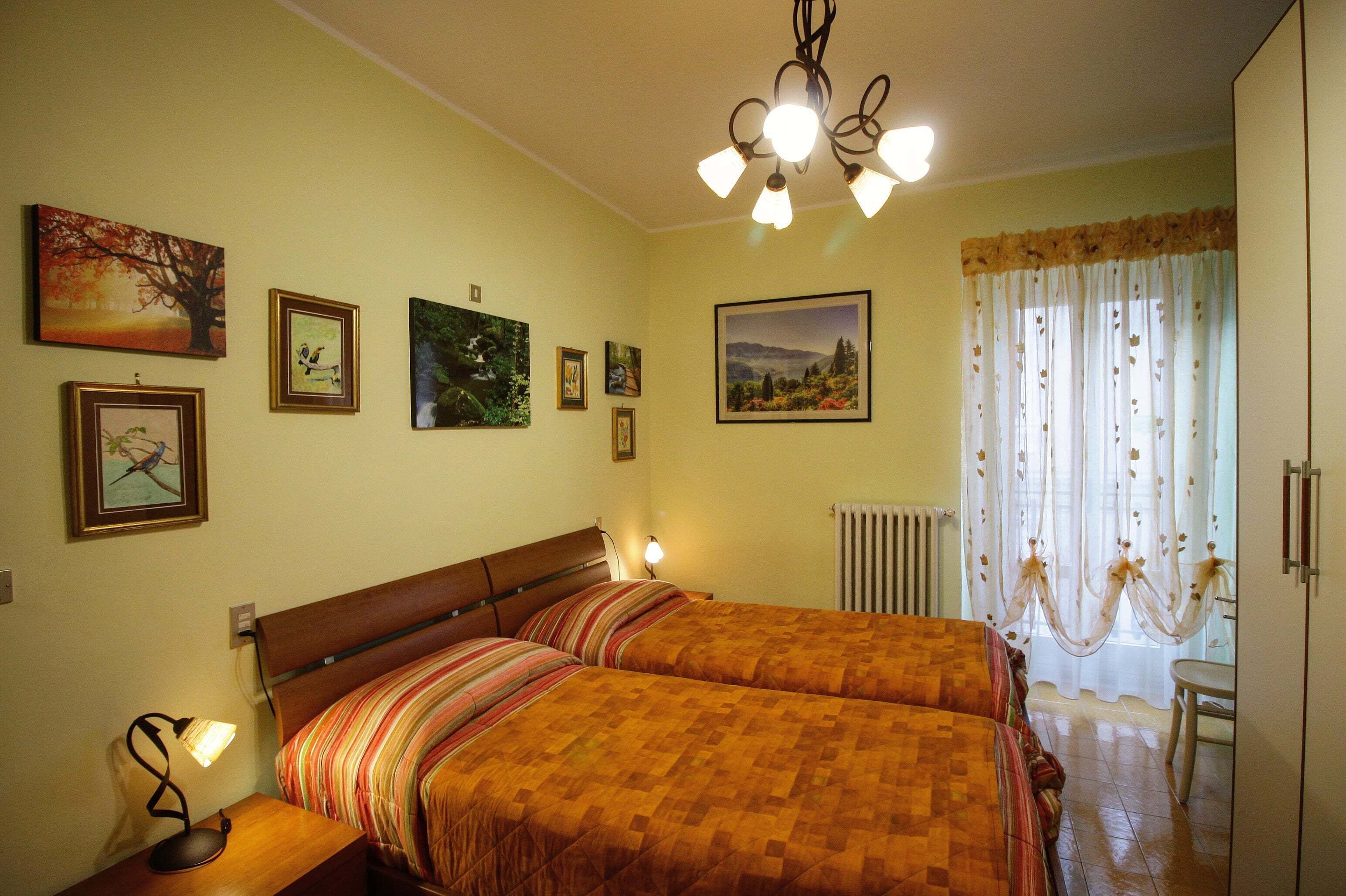 A bedroom with two beds, a chandelier, and several framed pictures on the wall.