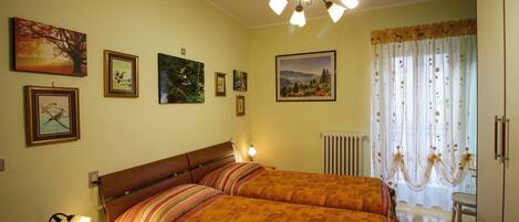 A bedroom with two beds, a chandelier, and several framed pictures on the wall.