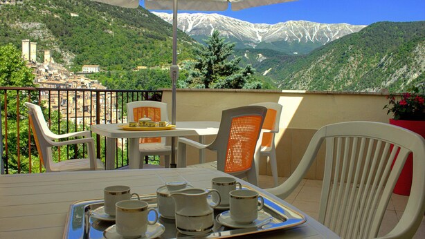 Une terrasse avec une table dressée pour le thé, des chaises et une vue sur des montagnes enneigées.
