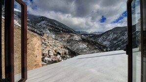 Vue depuis une chambre dotée d’une grande fenêtre donnant sur une montagne enneigée et une ville historique située en contrebas.