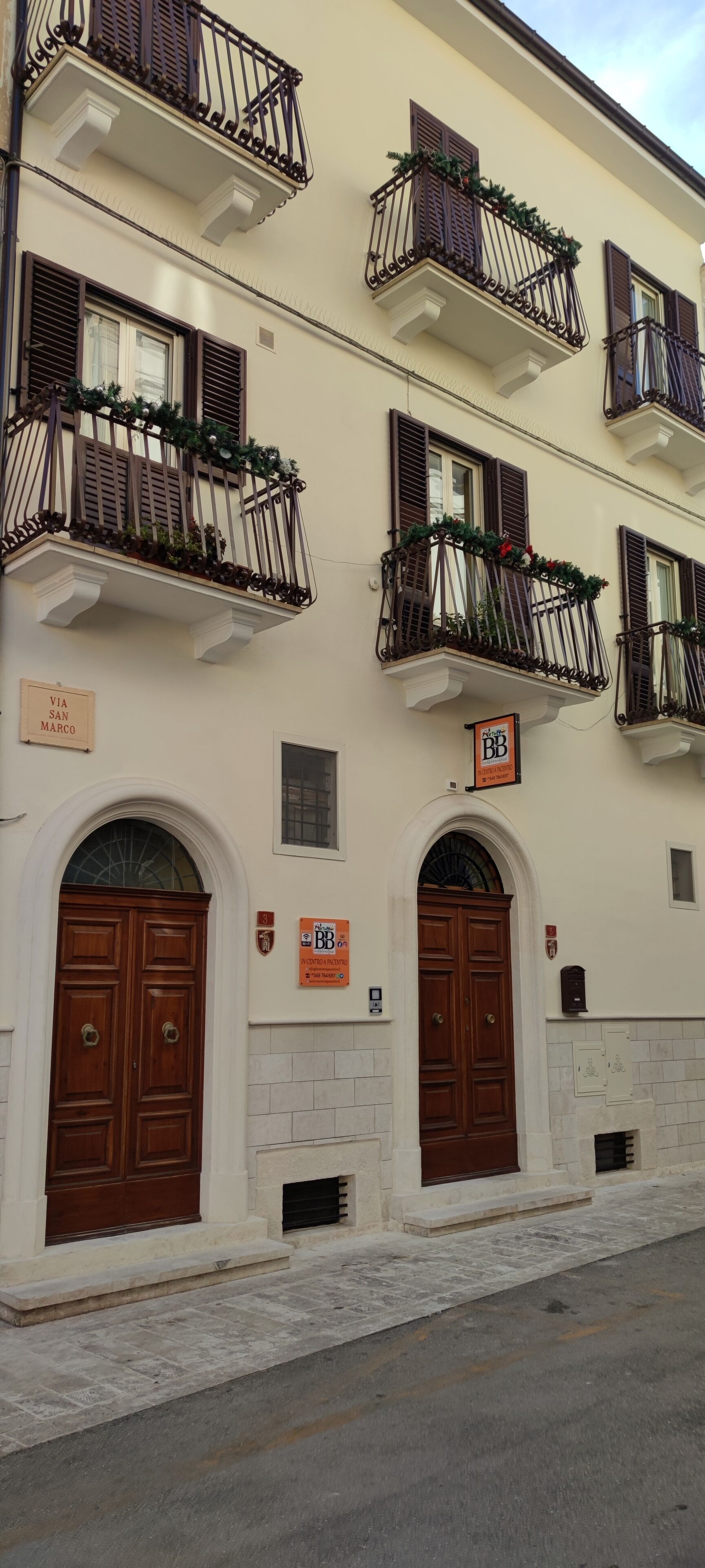 A building with multiple balconies, large wooden doors, and signs indicating room numbers and amenities.