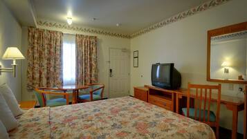 A hotel room with a bed, a desk with a television, a chair, and a lamp.