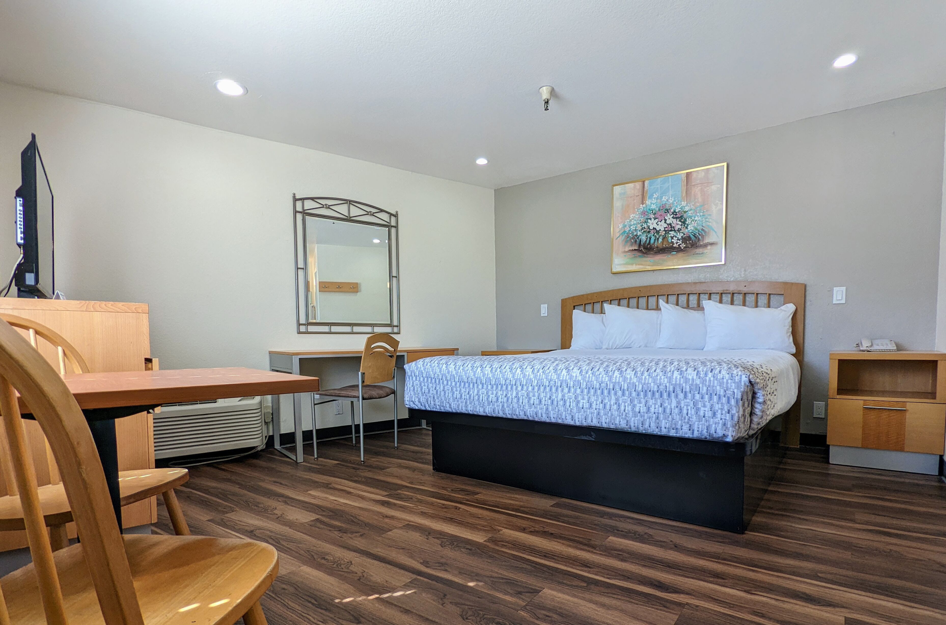 Una habitación de hotel con cama, escritorio, silla, televisor y un cuadro en la pared.
