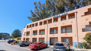 A hotel with multiple balconies and a parking lot with several cars. - Royal Inn (South San Francisco)